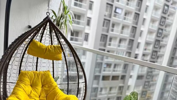 En balkon med en hængekøjsstol, et lille bord med drikkevarer og en potteplante.