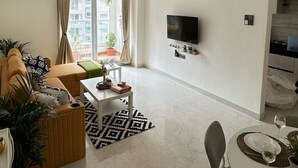 En moderne stue med sofa, sofabord, spisebord dækket til to personer, fjernsyn ophængt på væggen og en loftsvifte.