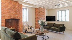 A living room with a brick fireplace, green sofas, a round coffee table, and a TV mounted on the wall. - Gardeners Cottage (Oakham)