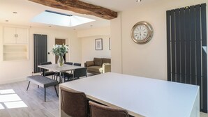 A modern dining area with a skylight, a clock on the wall, and a view of the outdoors. - Gardeners Cottage (Oakham)