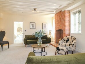 A living room with a green sofa, a round coffee table, a black and white patterned armchair, and a brick fireplace. - Gardeners Cottage (Oakham)