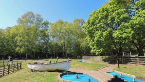 A boat named 'Angian Water' in a park with a small pond and a wooden fence. - Gardeners Cottage (Oakham)