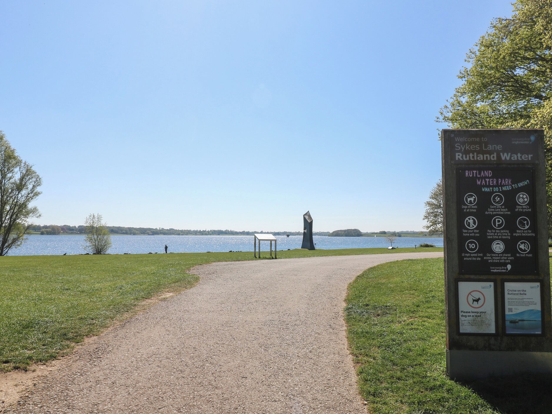 Un chemin de gravier mène à un plan d’eau, et un panneau d’information y est installé pour fournir des renseignements sur Sykes Lane et le réservoir de Rutland.