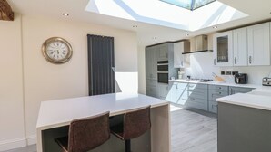 A modern kitchen with a skylight, a clock, and a bar area with stools. - Gardeners Cottage (Oakham)