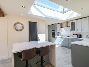 A modern kitchen with a skylight, a clock, and a bar area with stools. - Gardeners Cottage (Oakham)