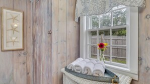 Une pièce aux murs en bois, une fenêtre donnant sur une clôture en bois, une étoile de mer encadrée en guise de décoration, et un plateau avec des serviettes roulées.