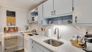 Une cuisine moderne avec des meubles blancs, un évier en acier inoxydable, une bouilloire et une machine à café.