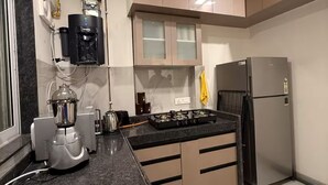 A modern kitchen with a built-in water dispenser, a gas stove, a refrigerator, and a ceiling fan. - Earthen Escape 2BHK near BKC Jio  Gym Access (Mumbai)