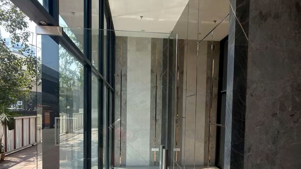 A modern building interior with large glass windows, a concrete floor, and a metal railing. - Earthen Escape 2BHK near BKC Jio  Gym Access (Mumbai)