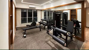 A gym with exercise equipment, a bench, and a mirrored wall. - Earthen Escape 2BHK near BKC Jio  Gym Access (Mumbai)
