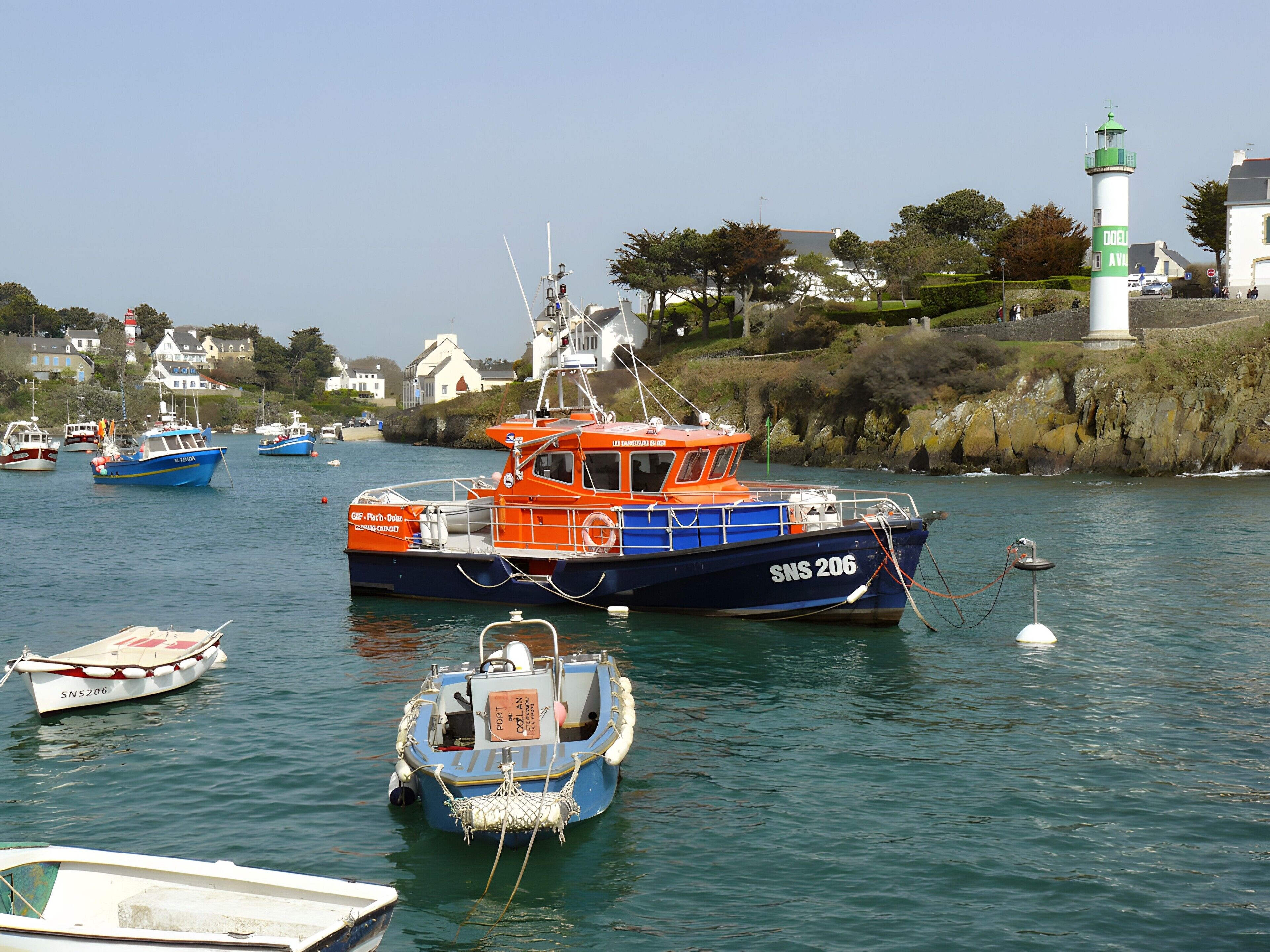 A harbor with boats, a lighthouse, and houses in the background.