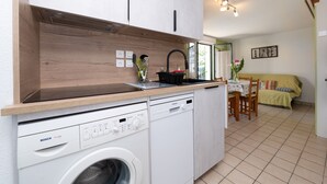 Una cocina compacta con lavadora Bosch, lavavajillas Siemens, armarios de madera y una zona de comedor con mesa y sillas.
