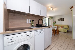 A compact kitchen with a Bosch washing machine, a Siemens dishwasher, wooden cabinets, and a dining area with a table and chairs. - Holiday Home “La Maison Du Haut Pouldu”: Sea View, Shared Pool, Private Terrace (Clohars-Carnoët)