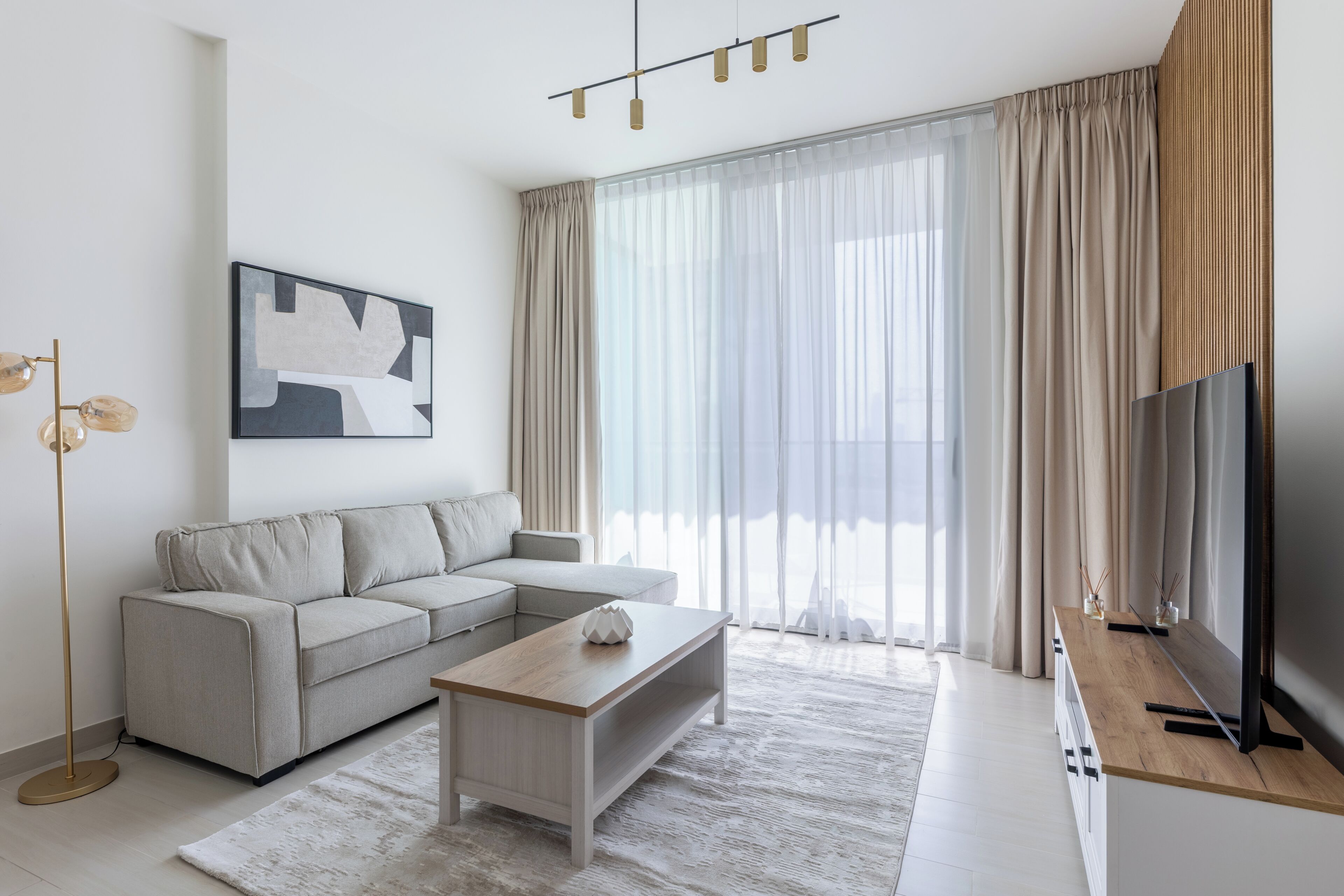 Un salon moderne avec un canapé, une table basse, un téléviseur et de grandes fenêtres dotées de rideaux.