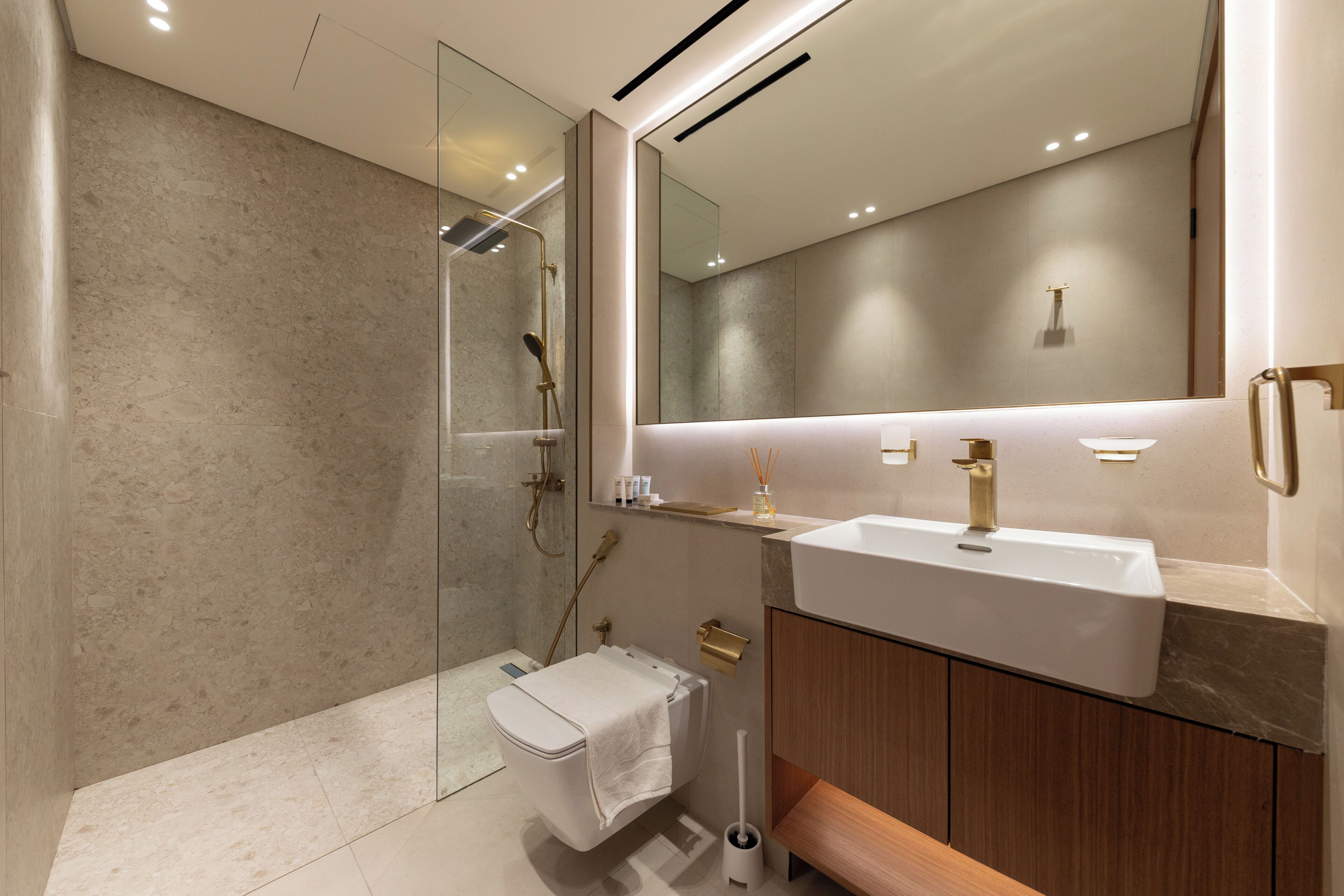 A modern bathroom with a glass shower enclosure, a white toilet, a wooden vanity with a white sink, and a large mirror.