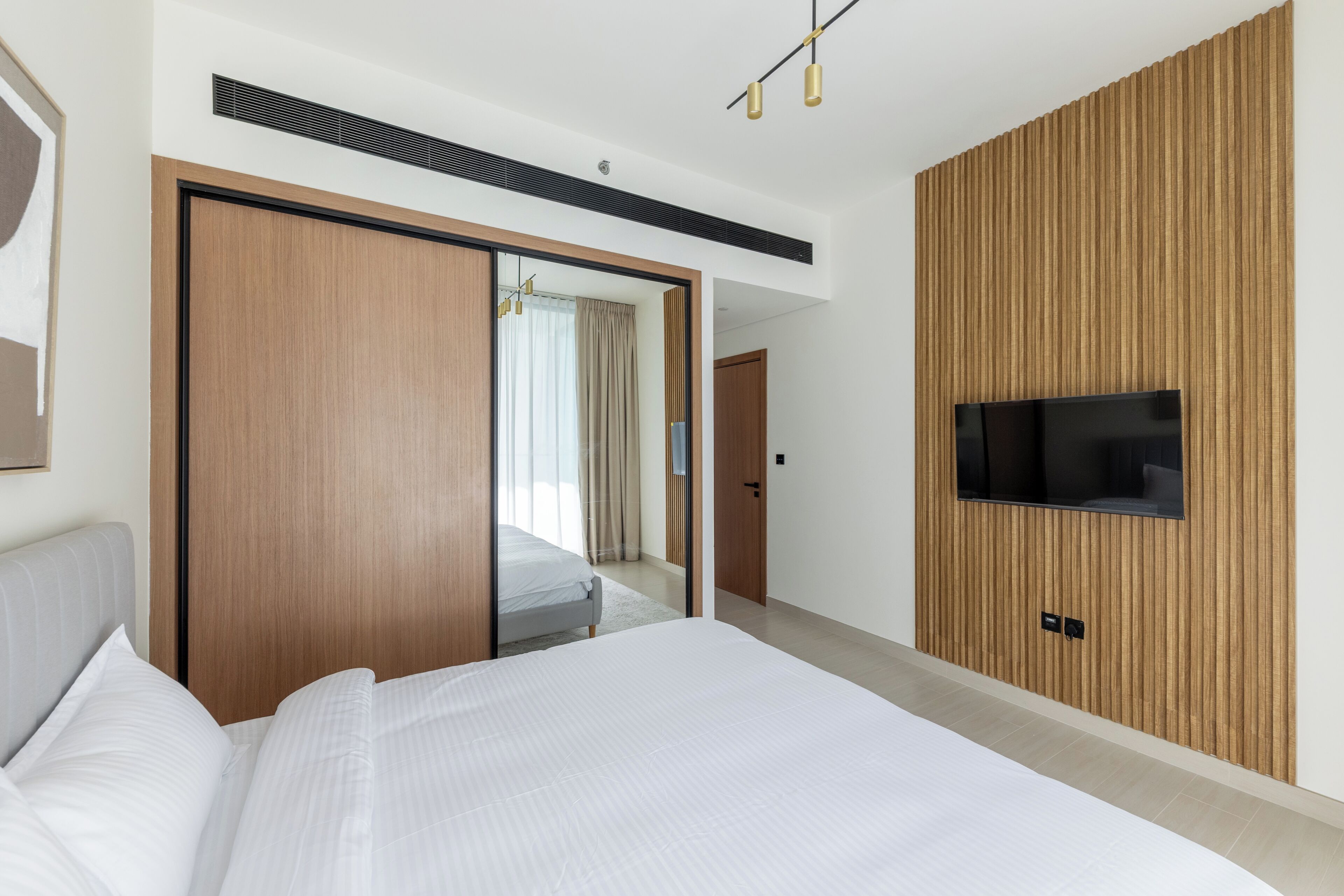 Une chambre d’hôtel moderne avec un grand lit, un téléviseur fixé sur un mur recouvert de panneaux en bois et un placard à portes coulissantes.
