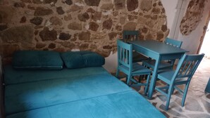 Una stanza con una parete in pietra, un divano color petrolio e un tavolo e sedie abbinati.