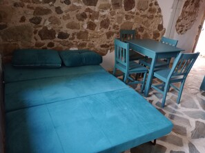 Um quarto com parede de pedra, sofá verde-esmeralda e mesa e cadeiras combinando.