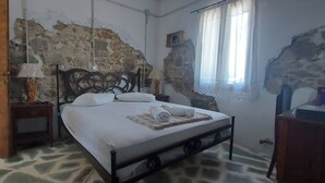 Una camera da letto con una parete in pietra, un letto con lenzuola bianche, una porta di legno e un pavimento a motivi.