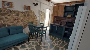 Una stanza con parete in pietra, un divano color petrolio, un tavolo da pranzo con sedie e un angolo cottura con mobili in legno e un frigorifero.