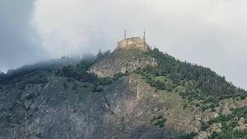 Ein Berg mit einem Gebäude auf der Spitze, umgeben von Bäumen und felsigem Gelände.