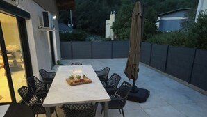 Un patio al aire libre con una mesa y sillas, una sombrilla y vistas a una colina.