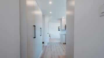 A modern hallway with white walls, wooden flooring, and recessed ceiling lights.