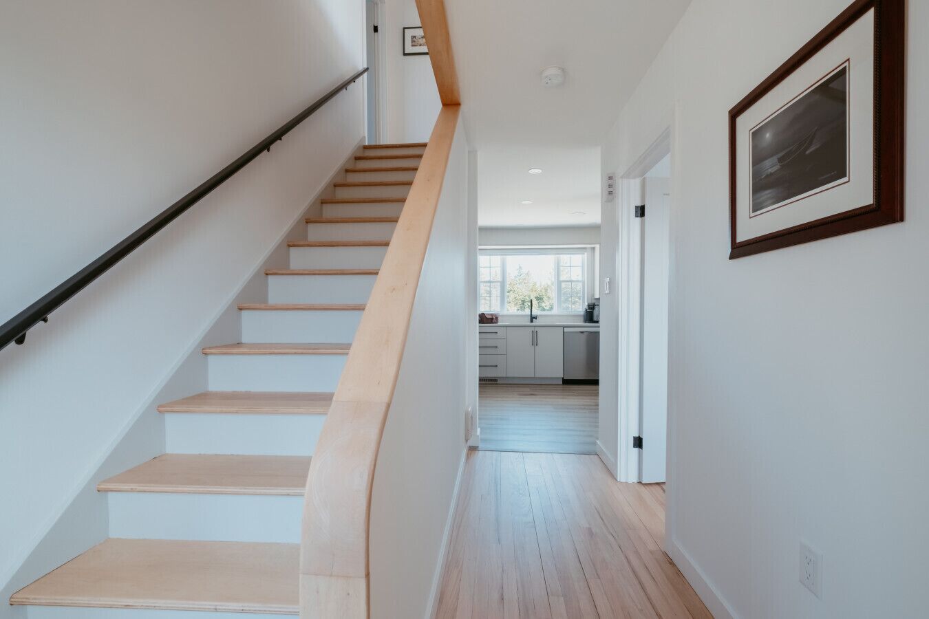 A staircase leading to a kitchen with white cabinets and a window.