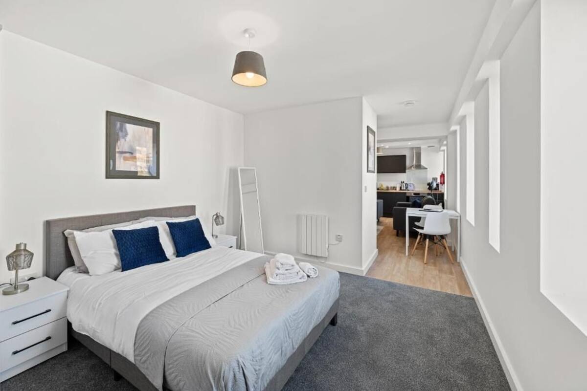 A modern bedroom with a bed, bedside table, and a desk in the adjacent room.