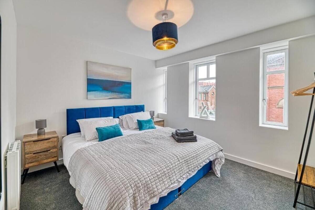 A bedroom with a bed, a nightstand, a lamp, a painting, and a window.