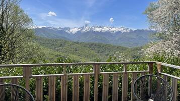 Une terrasse en bois avec deux chaises, une vue sur des montagnes enneigées et une forêt verdoyante.