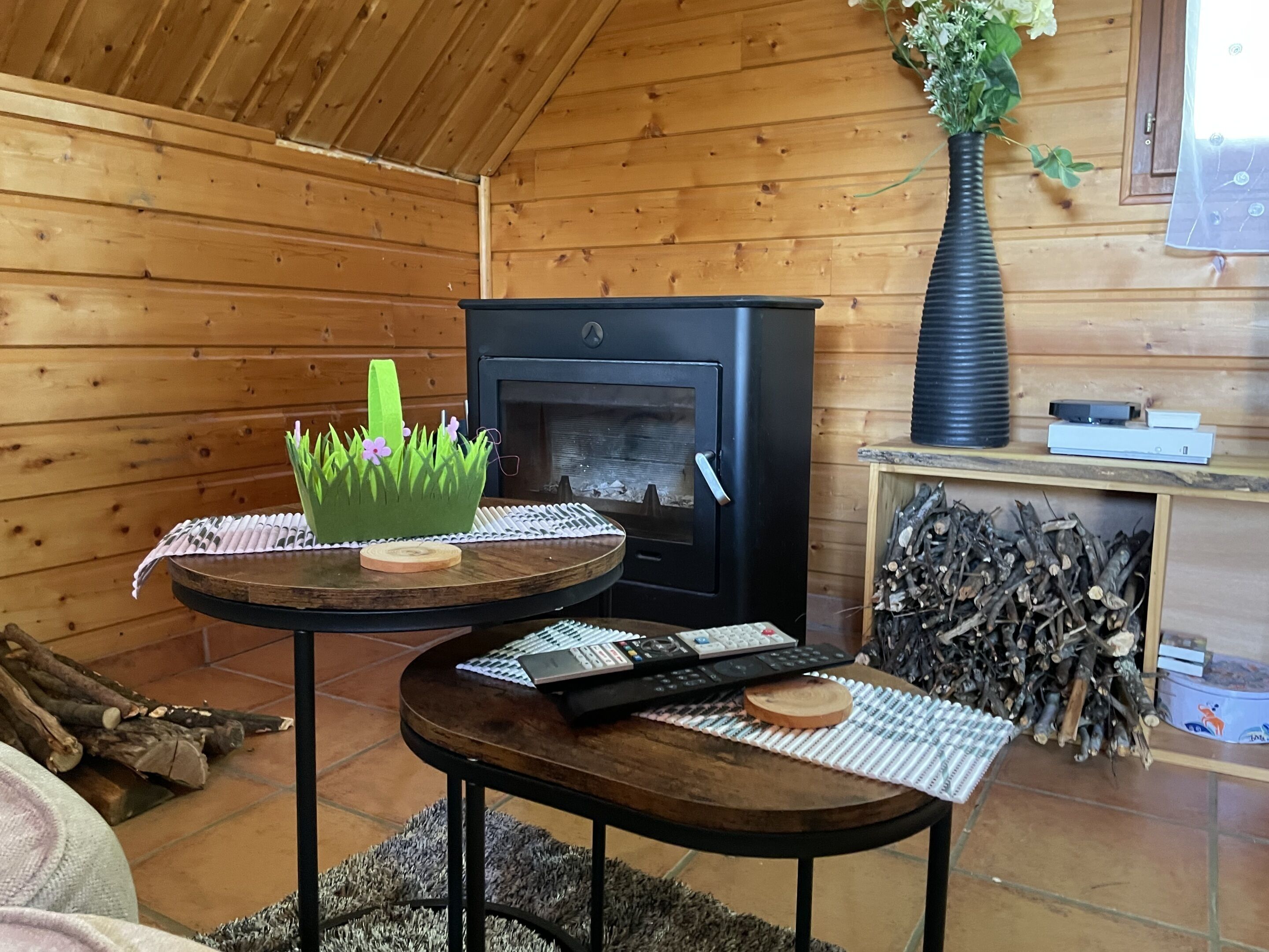 A cozy wooden cabin interior with a fireplace, a round table with a keyboard, and a decorative plant.