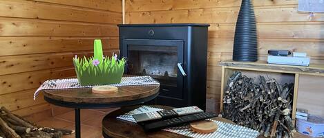 A cozy wooden cabin interior with a fireplace, a round table with a keyboard, and a decorative plant.