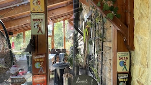 A rustic wooden building with a stone wall, a welcome sign, and multiple Le Routard recommended signs from 2020 to 2026.