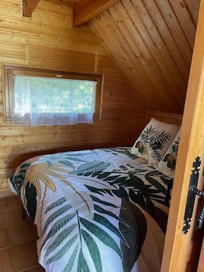 Een slaapkamer in een houten hut met een bed, een raam en een deur.