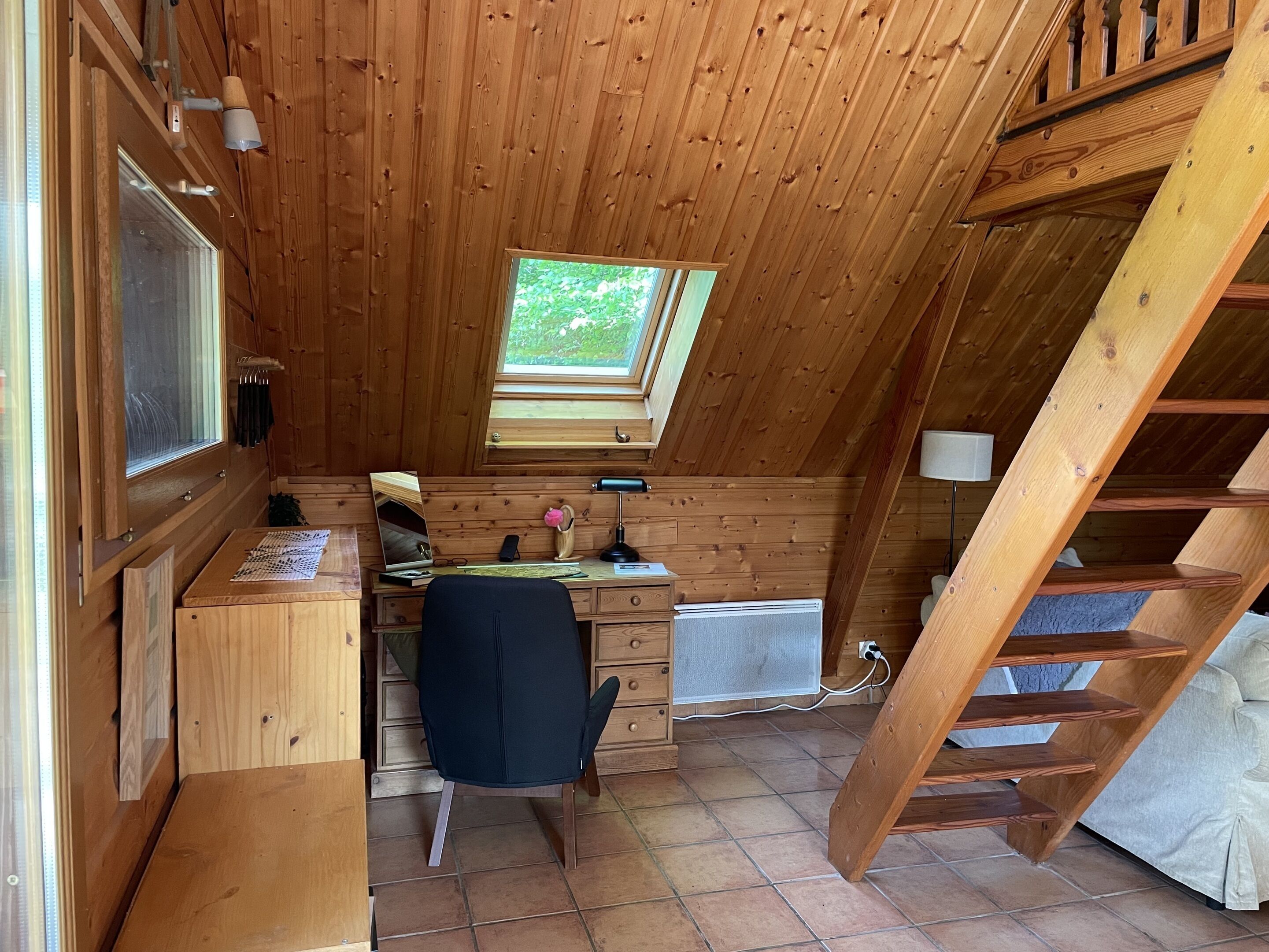 Une cabane en bois avec un bureau, une chaise et une fenêtre donnant sur la verdure.