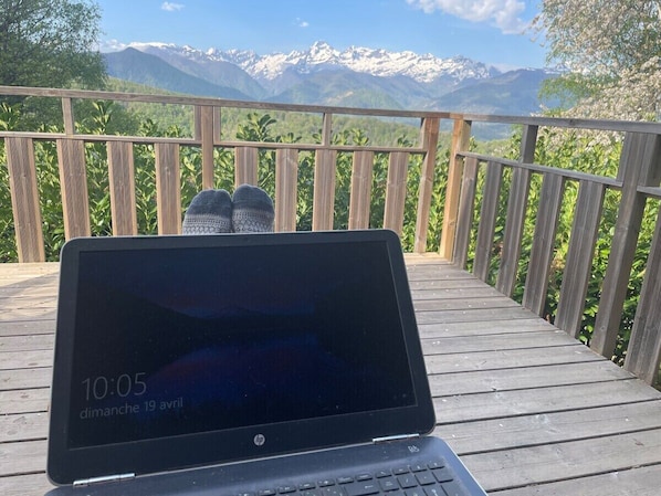 A laptop on a wooden deck with a mountain view.