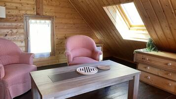 Una habitación acogedora con paredes de madera y techo inclinado, que incluye un sillón a cuadros, una mesita con un plato decorativo y un aparador de madera.