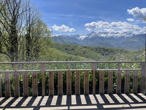 Una terraza de madera con vistas a montañas nevadas y un valle boscoso.