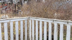 Eine Holzdielen-Terrasse mit senkrechten Geländern, umgeben von dichtem Buschwerk und Bäumen.