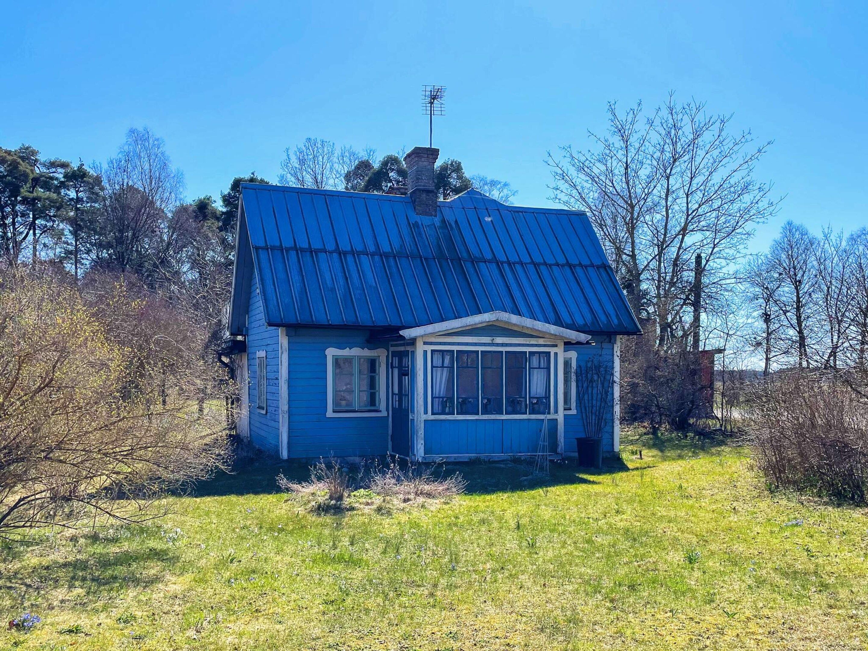 A small house with a blue roof and a chimney, surrounded by trees and grass.