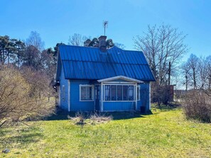 A small house with a blue roof and a chimney, surrounded by trees and grass. - 7 Person Holiday Home in Stanga (Stånga)