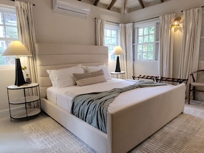 Ein Schlafzimmer mit einem großen Bett, zwei Nachttischen, einem Sessel und einem Fenster mit Vorhängen.