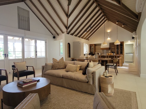 A spacious living area with a high ceiling, a sofa, a coffee table, and a kitchen in the background.