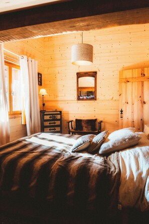 A wooden cabin-style room with a bed, a dresser, a mirror, and a hanging light fixture. - Chalet in the mountains, ideal for families! (Bolquère)