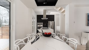 Una cocina moderna con una isla central, sillas blancas y un bol negro con manzanas.