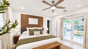 Ein Schlafzimmer mit Bett, Nachttischen, Deckenventilator und Blick auf einen Pool durch die Schiebetür.