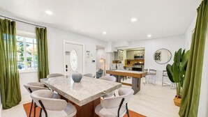 Ein modernes Wohnzimmer mit einem Esstisch aus Marmor, bequemen Sitzgelegenheiten, einem Billardtisch und einer Küchenzeile.