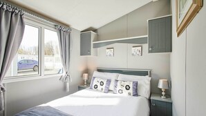 Een slaapkamer met een bed, nachtkastjes, een raam met gordijnen en uitzicht op een parkeerplaats.