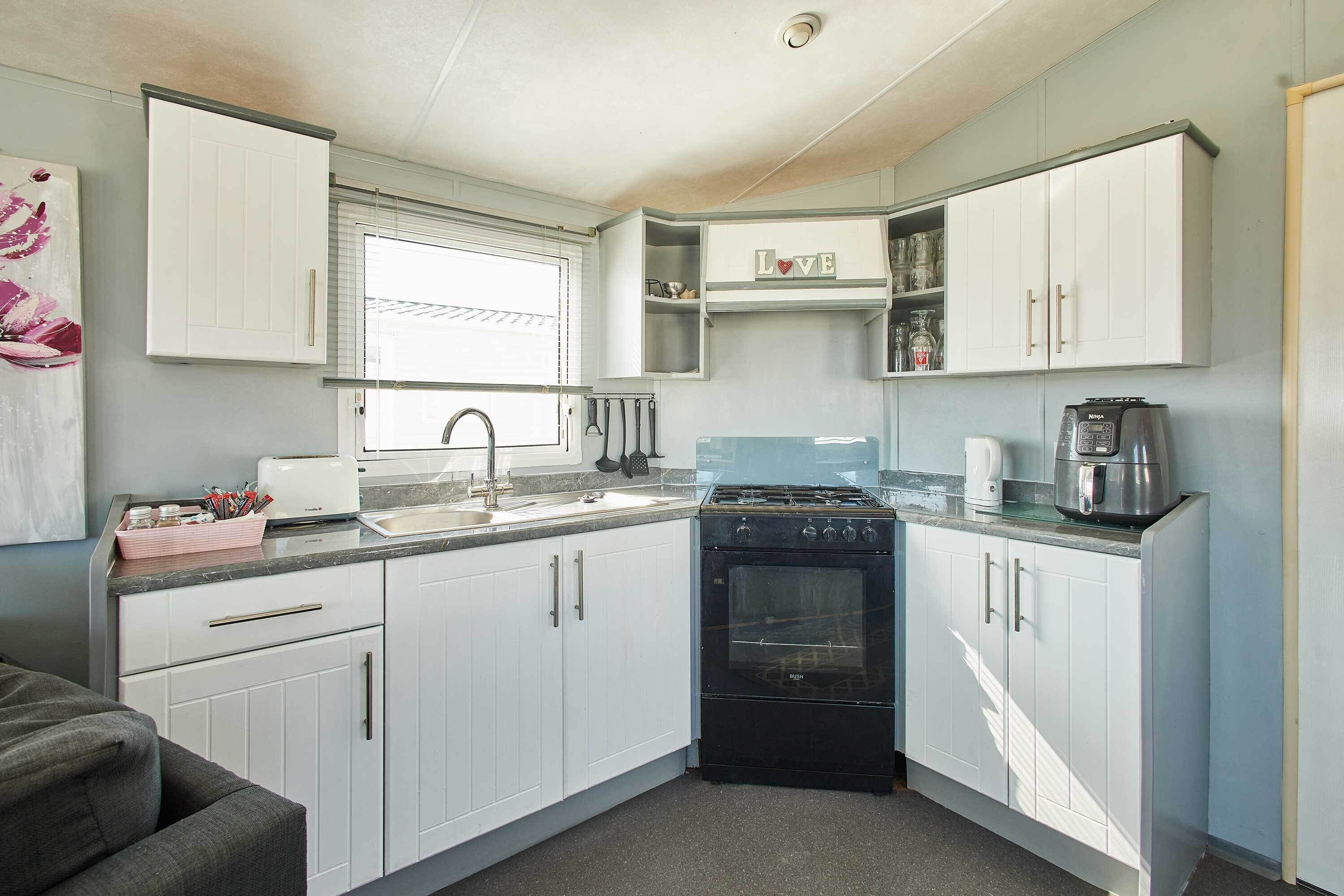 A compact kitchen with white cabinets, a black stove, a coffee maker, and a window with blinds.